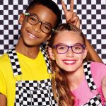 Two happy children wearing multi-coloured eyeglass frames on a checkered background